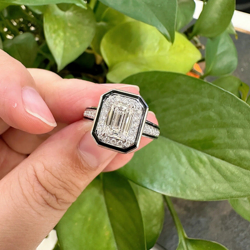 Diamond ring held between fingers with green leaves in the background