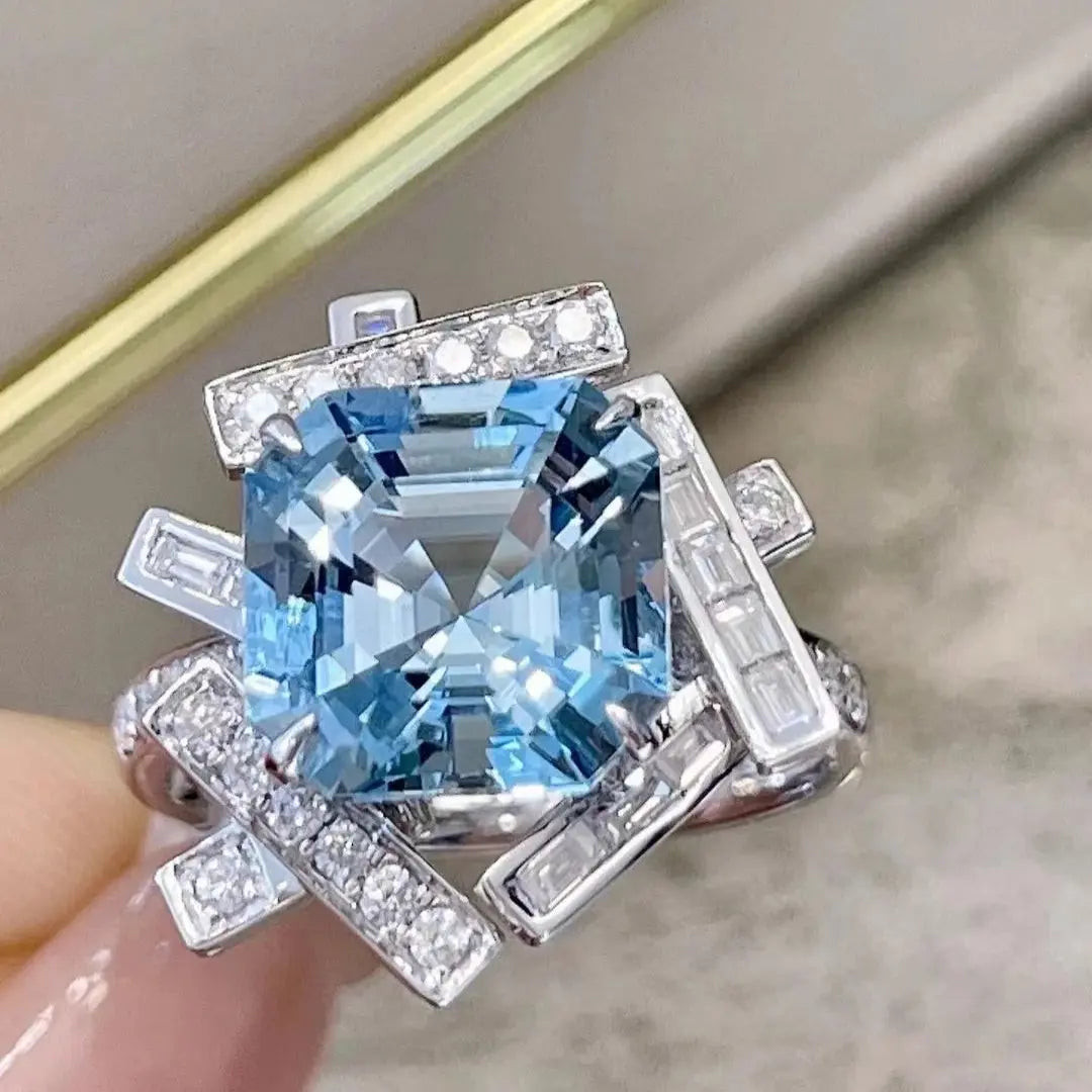 Ring with blue gemstone and diamond accents held by a hand against a neutral background