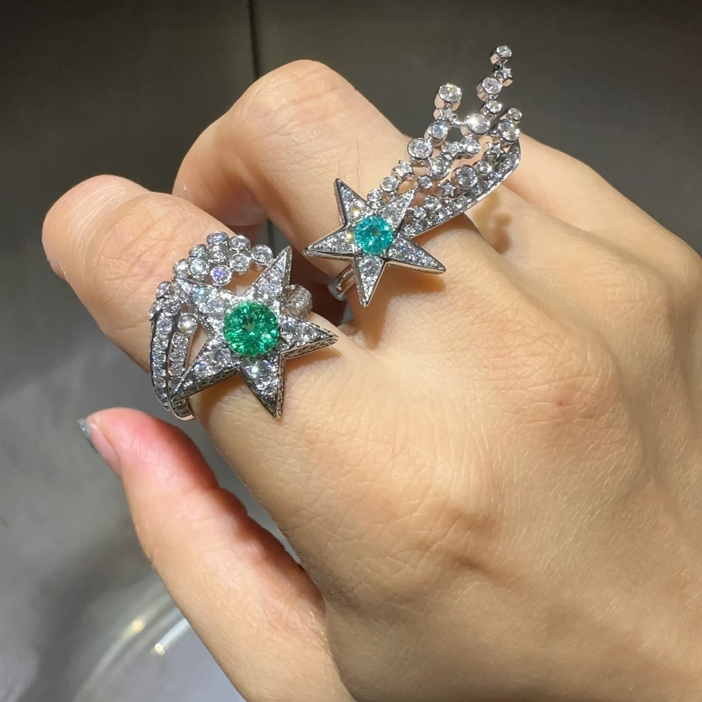 Two star-shaped earrings with gemstones on a hand against a neutral background