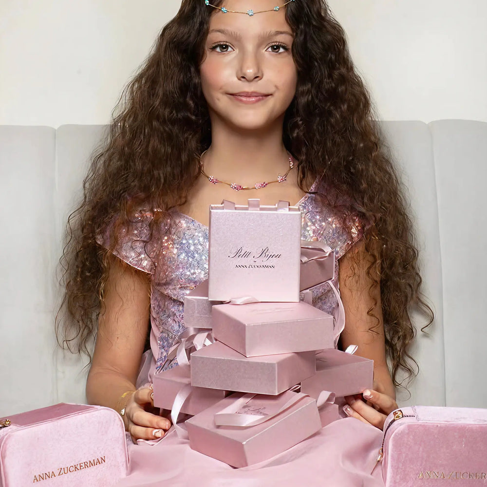 Young girl holding a stack of pink jewelry boxes with 'Anna Zuckerman' branding.
