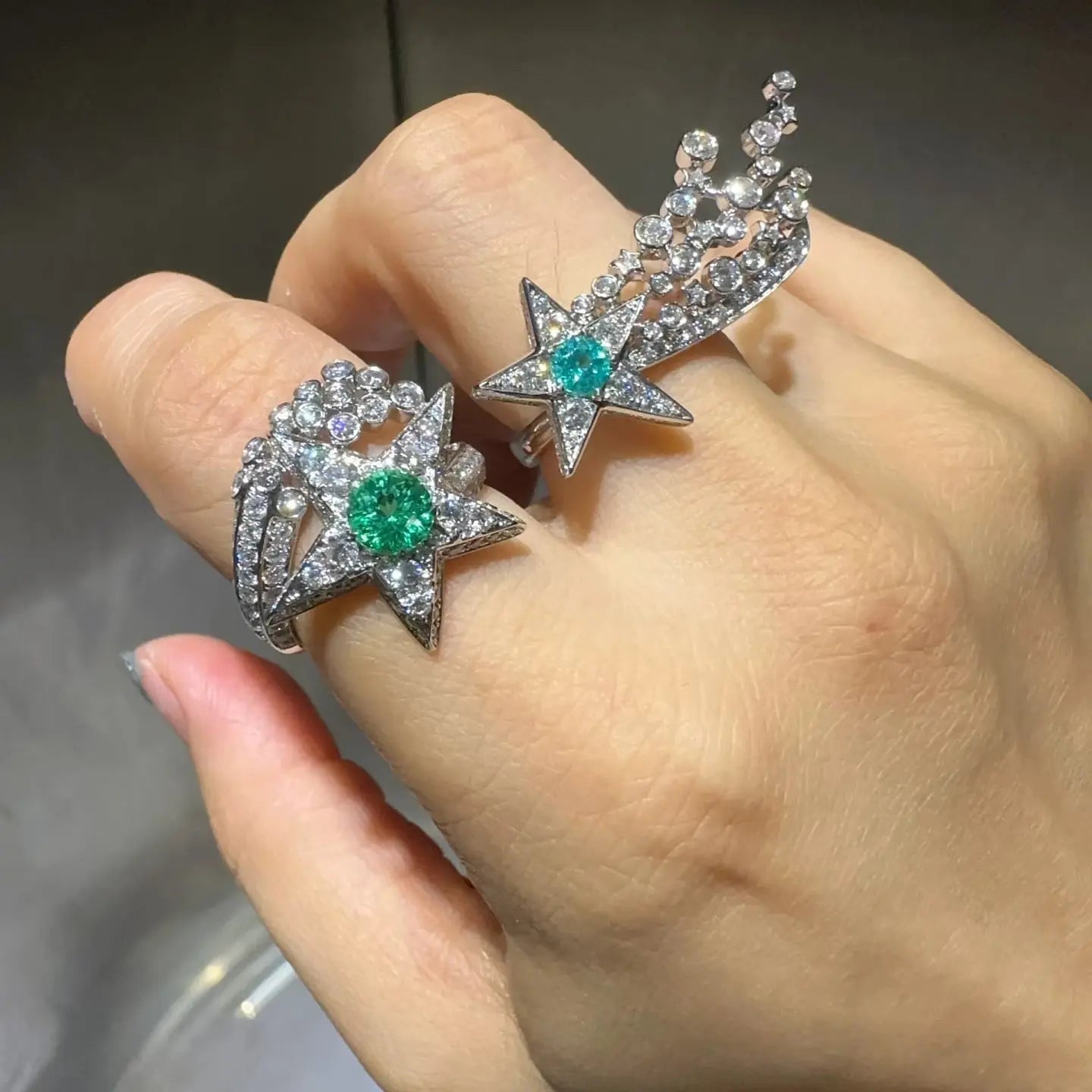 Two star-shaped earrings with gemstones on a hand against a neutral background