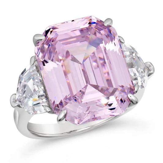 A cocktail ring with a large argyle pink crystalline gemstone in the center, flanked by smaller clear crystals on a silver metal band.